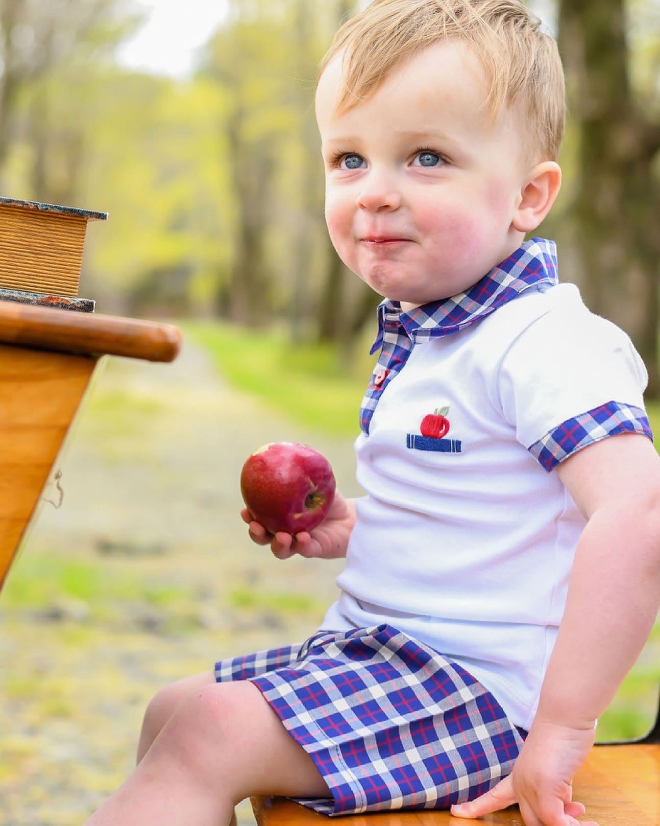 Model is sitting at a desk outside eating apple while wearing Apple of my Eye Boys Polo and Apple of my Eye shorts. Shorts sold separately.